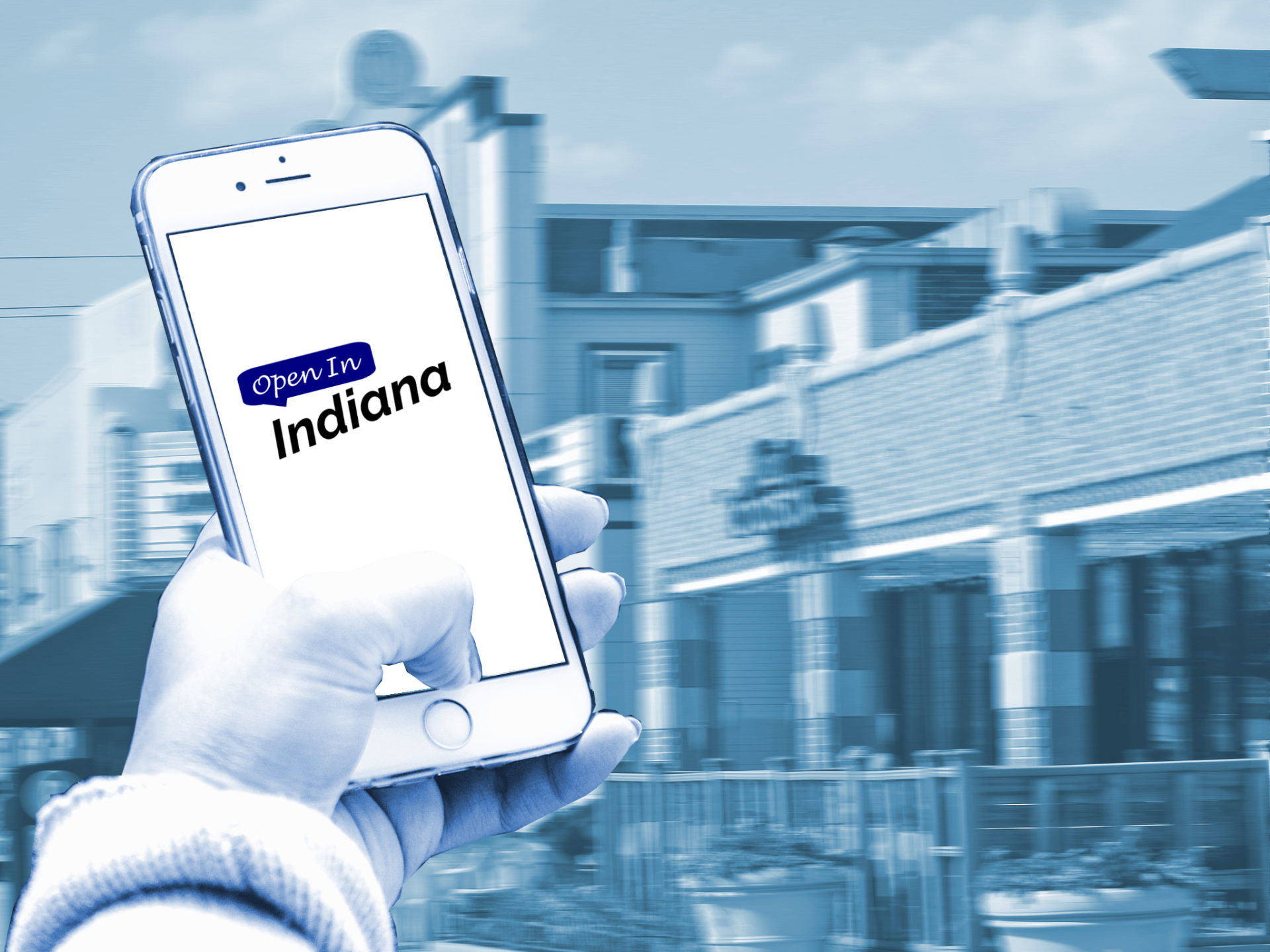 A person holding a smartphone with the Open In Indiana logo on it, in front of the strip in Broad Ripple.
